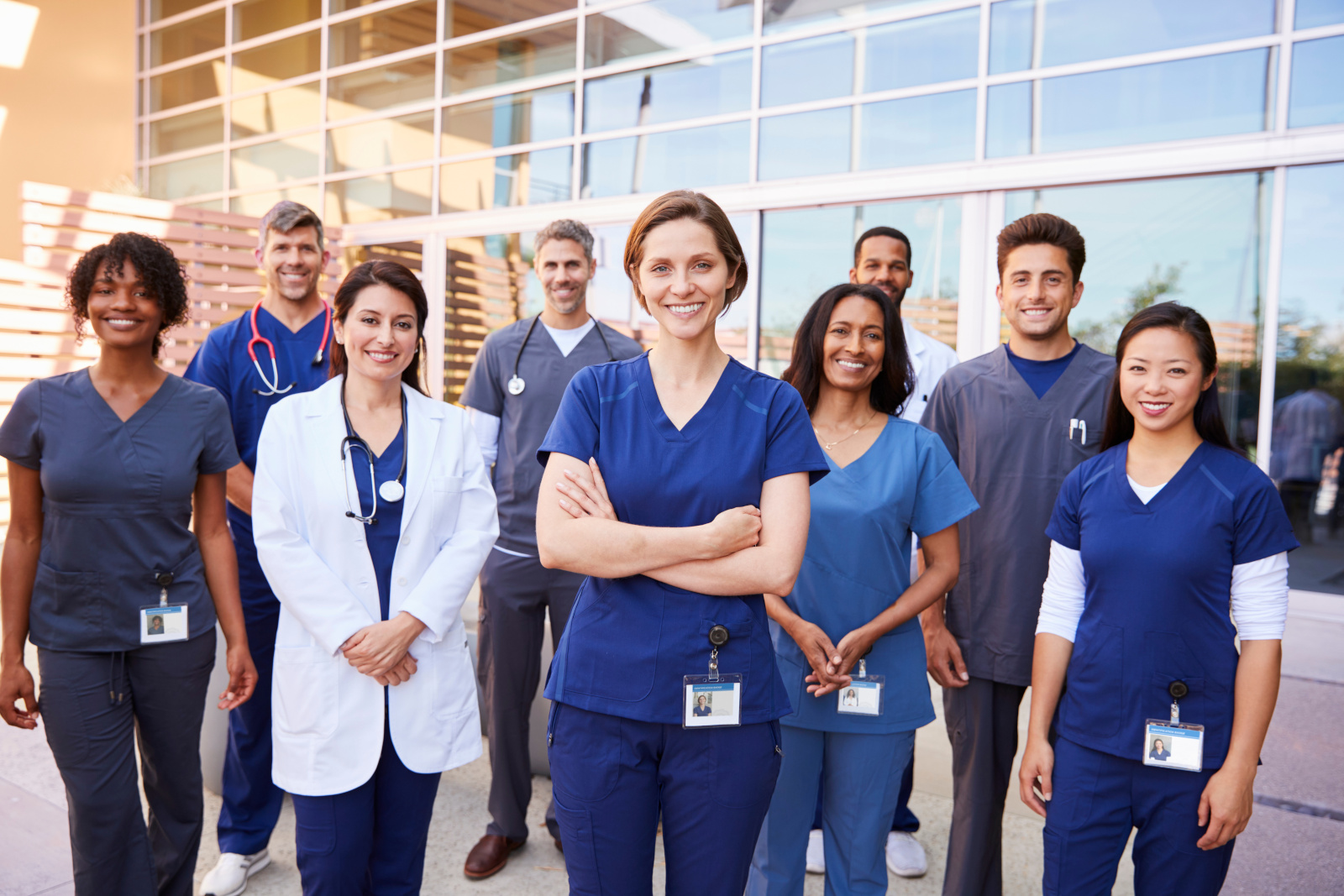 Team of healthcare workers with ID badges outside hospital A group of happy temporary nursing staff: Qualified, certified and compliant to work with YouRecruit and WorkTracker